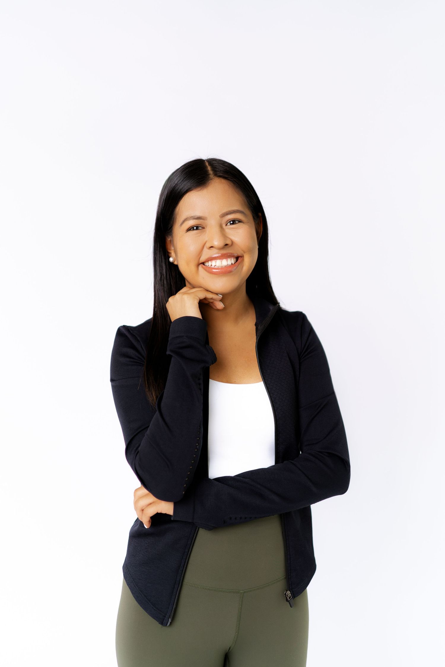Smiling young woman in black blazer and white top posing confidently against white background.