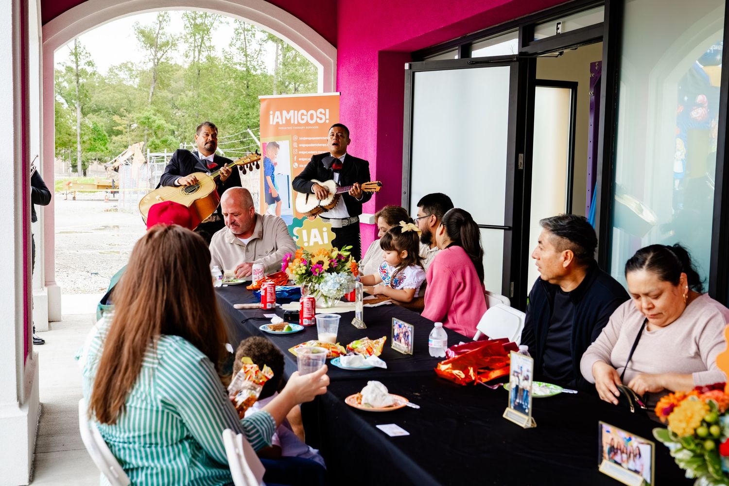 People gathered inside a building with pink accent walls and arched windows for a community event.