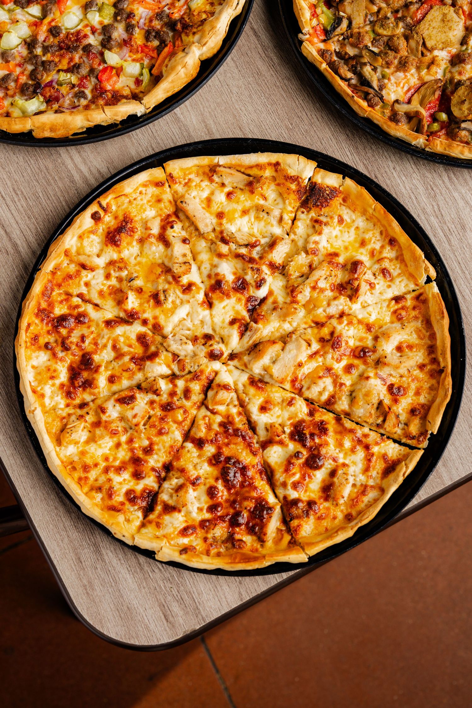 Overhead view of freshly baked pizzas with melted cheese and various toppings arranged in a row on dark surface.