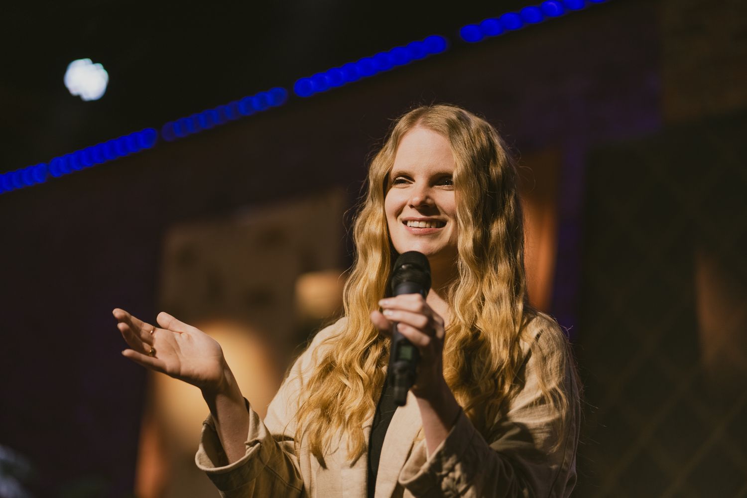 A performer singing passionately on stage with blue lighting effects.