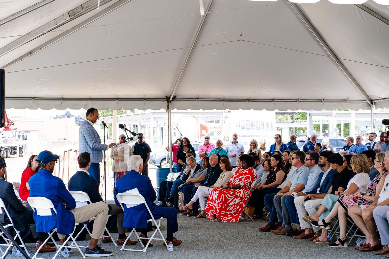 Large crowd seated under white outdoor tent during community gathering or event.