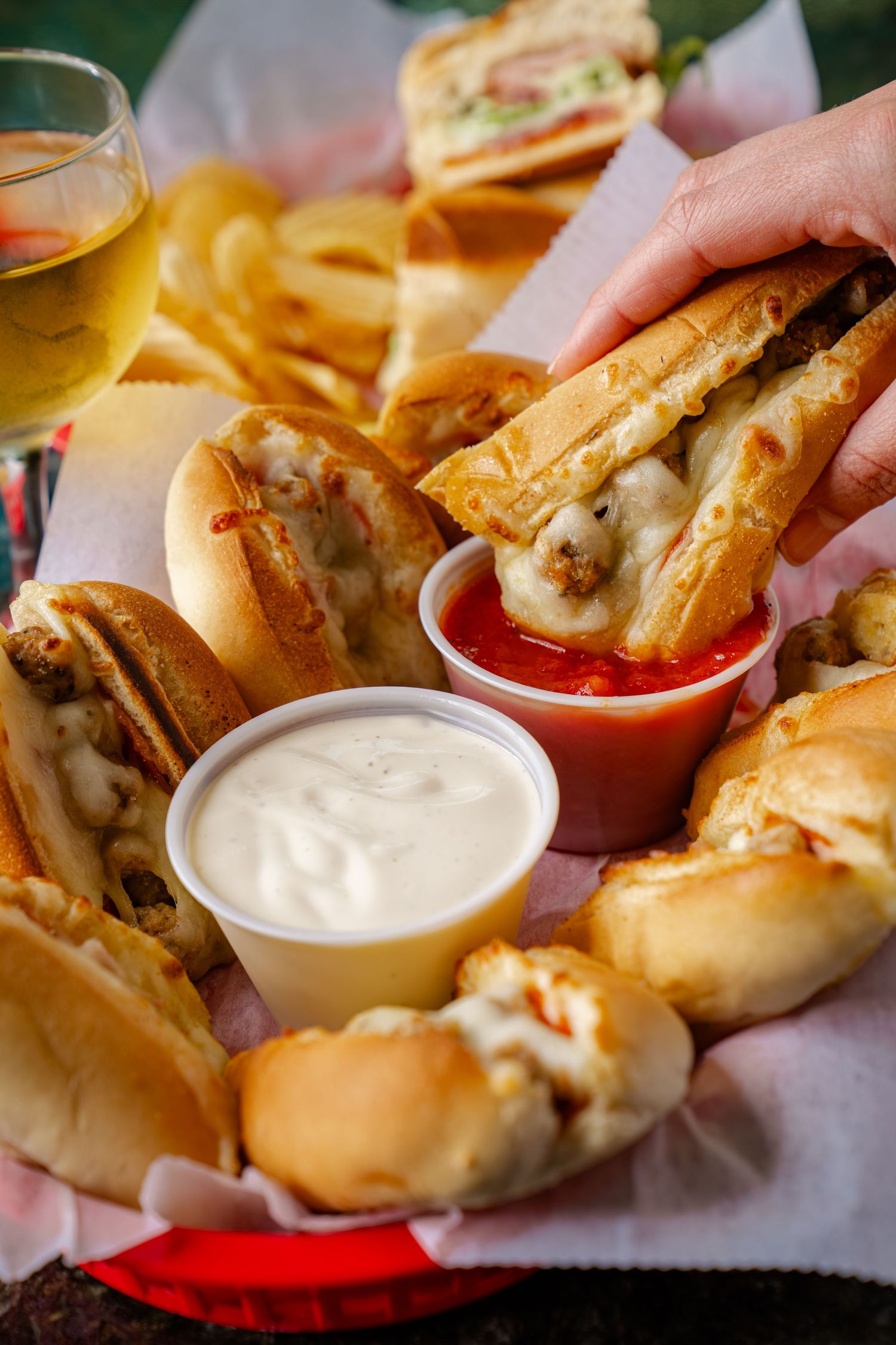 Mini sandwiches served with white and red dipping sauces alongside french fries and beer.