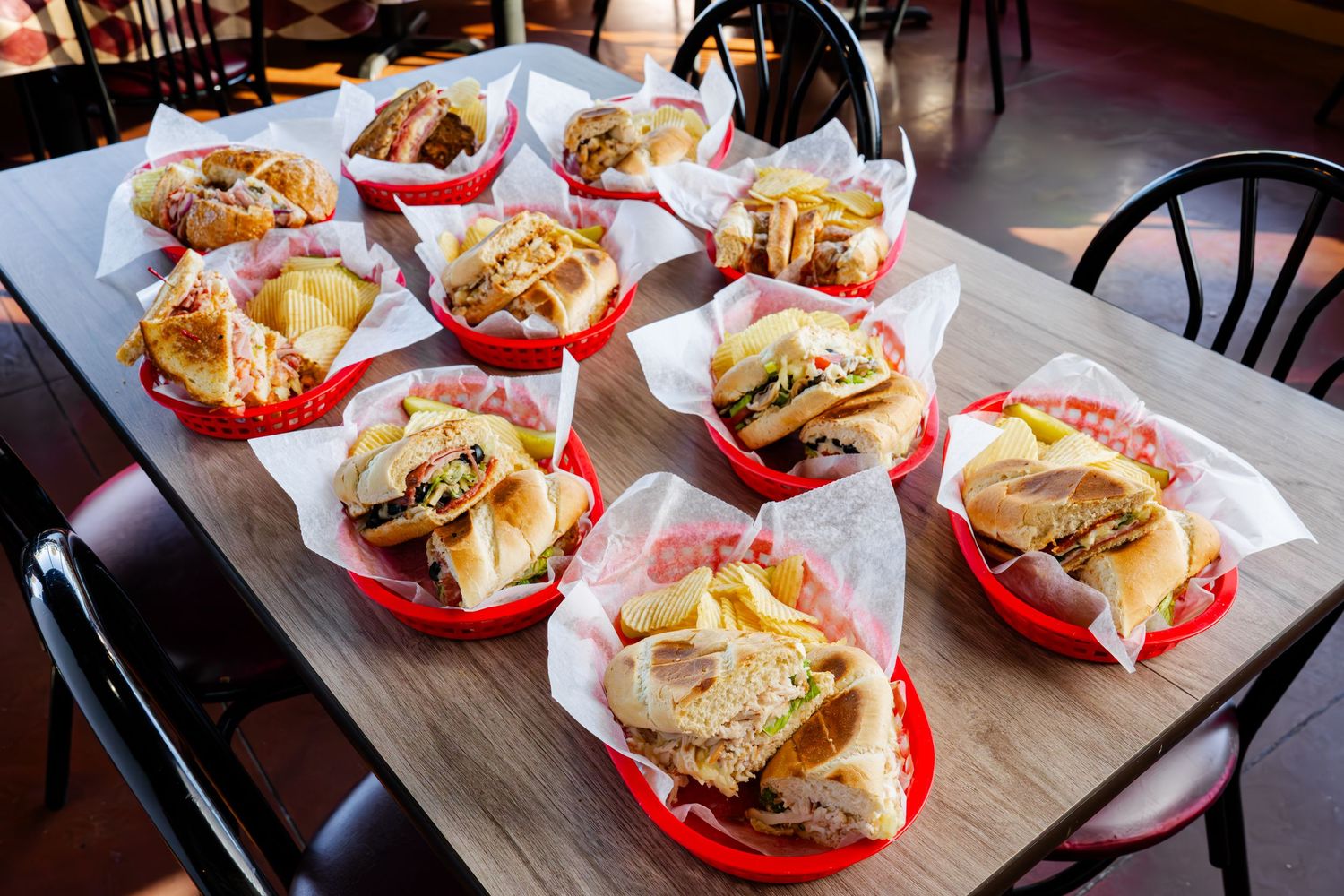 Red plastic baskets filled with grilled sandwiches and french fries lined up on a wooden restaurant table.