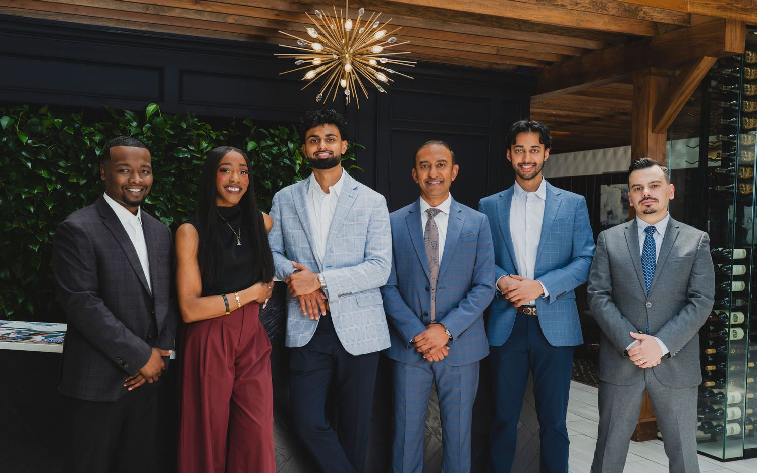 Six professionals in formal attire smiling together at an elegant indoor event venue.