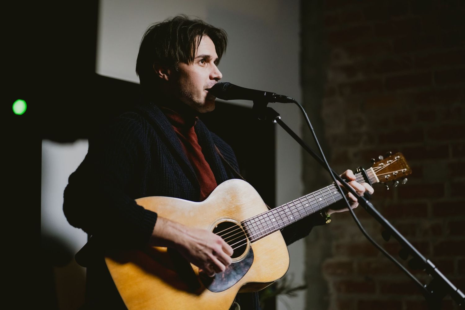 Acoustic guitar performance in dimly lit venue with spotlight.