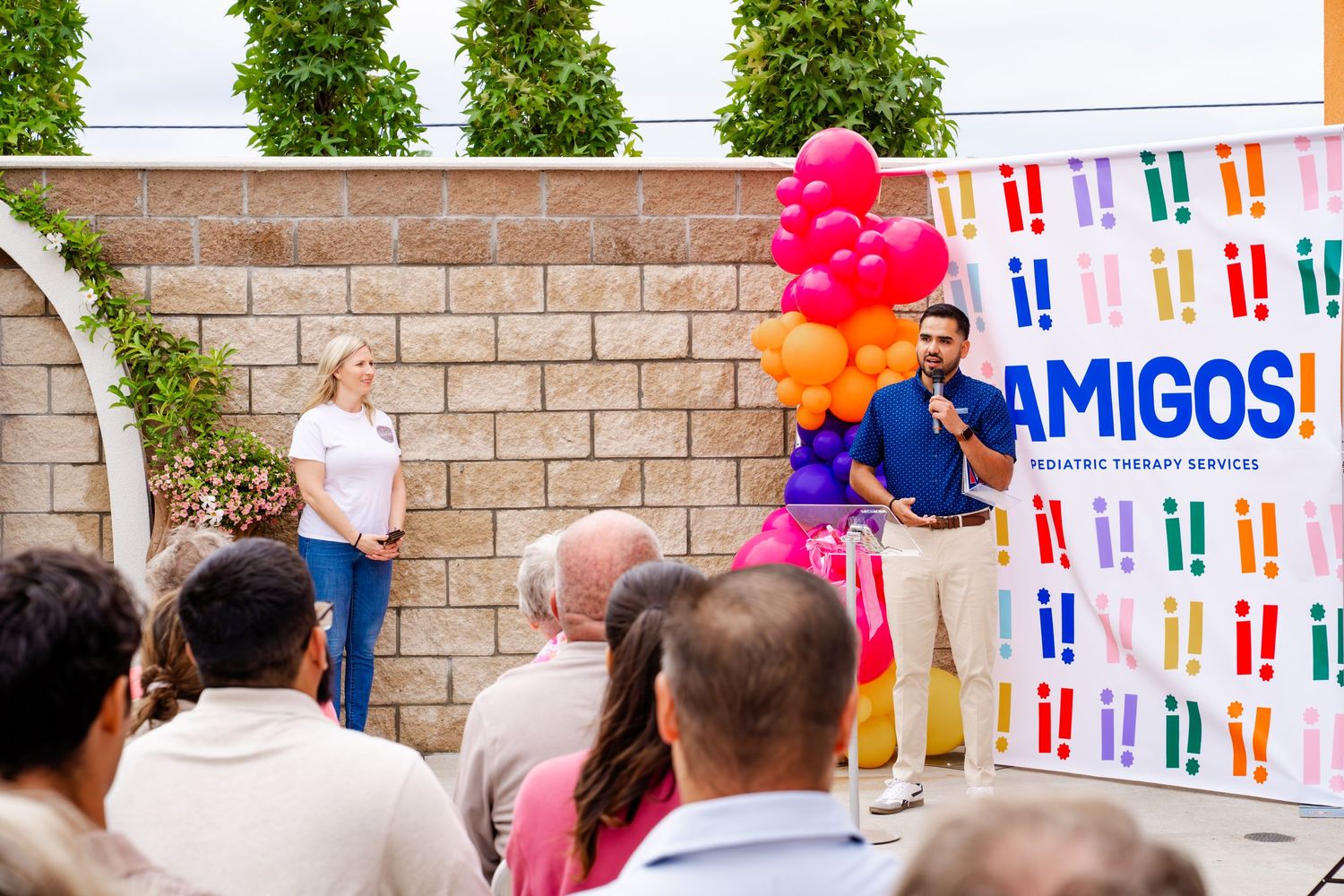 Outdoor gathering with colorful balloon arrangements and branded banners against building exterior.