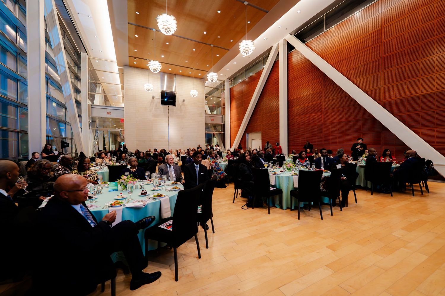 Large modern event space with round tables and architectural features hosting a formal gathering.