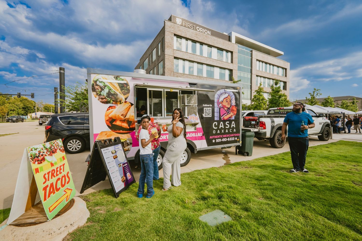 Outdoor festival with food trucks and vendor booths lined up on grassy area.