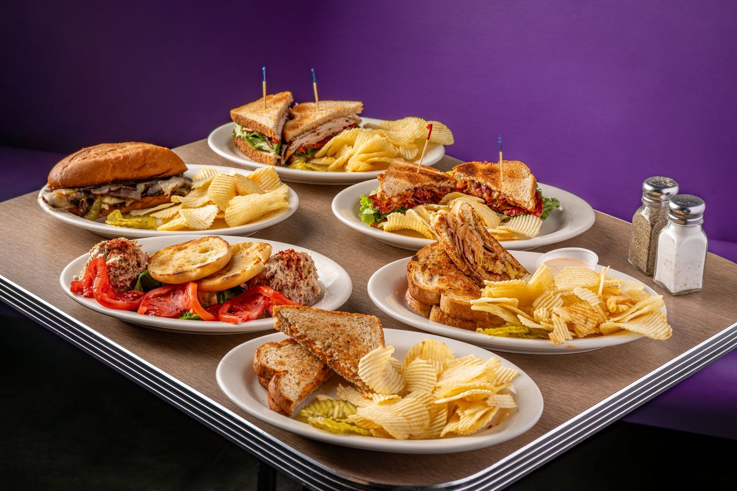 Row of plated sandwiches and fries on purple-lit restaurant counter.