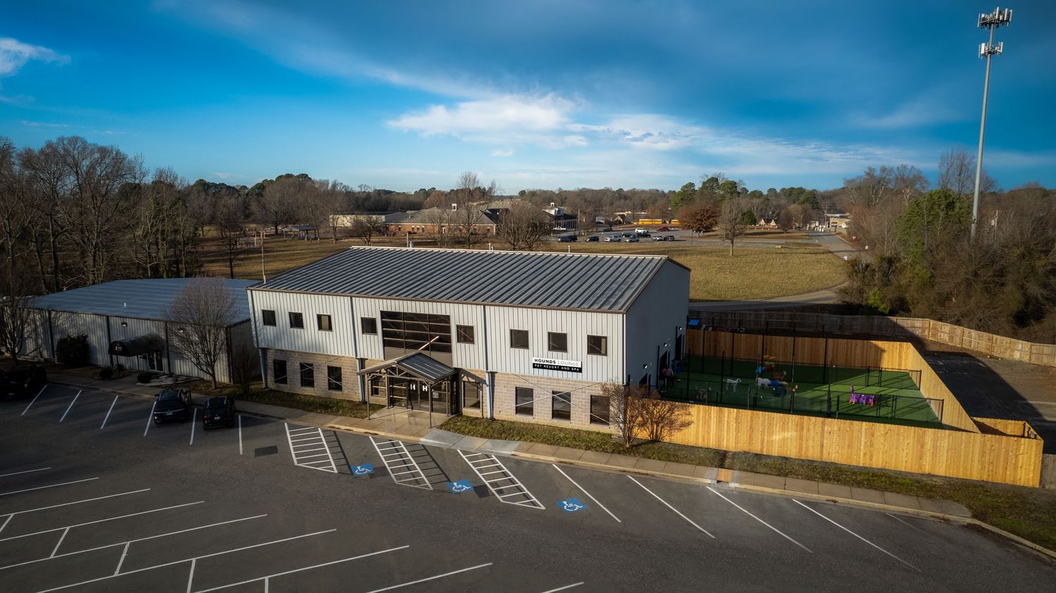 Aerial view of commercial building with parking lot and fenced area on sunny day.
