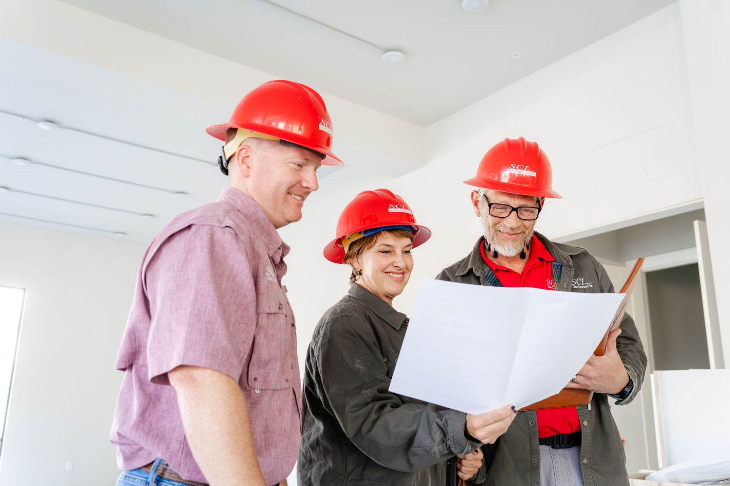 Group of construction workers in red hard hats reviewing building plans together.