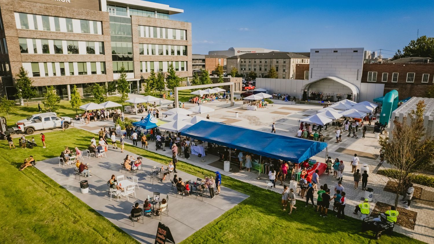 Panoramic view of an outdoor event space with vendor tents and crowds gathering under blue skies.