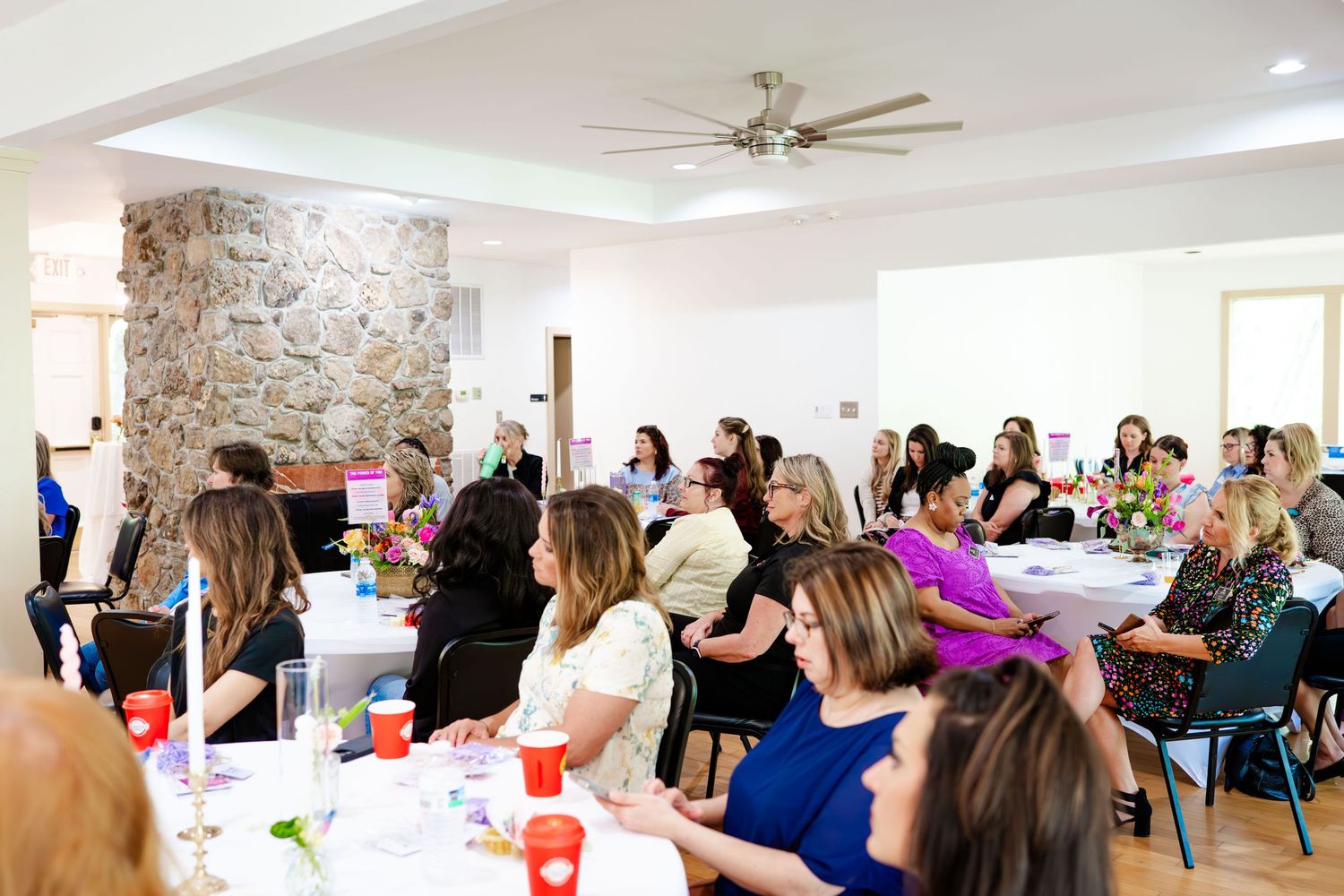 Large group meeting in modern venue with stone accent wall and rows of seating.