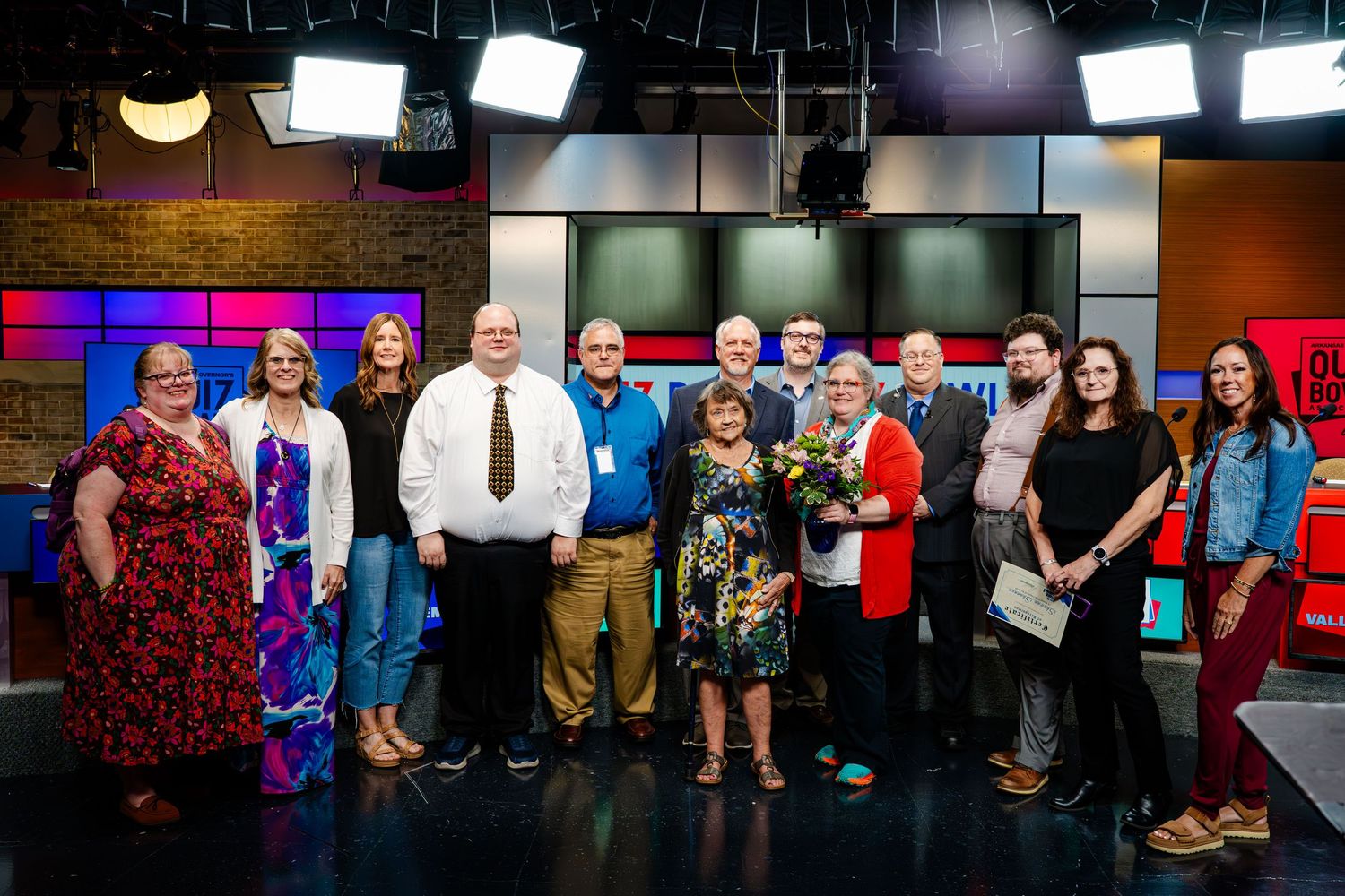 Group photo of participants lined up against a wall with studio lighting.