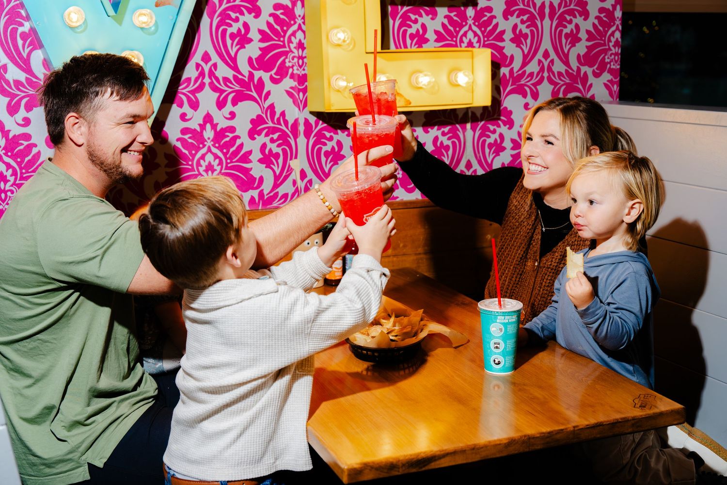 Happy family dining moment at restaurant with pink wallpaper and casual atmosphere.