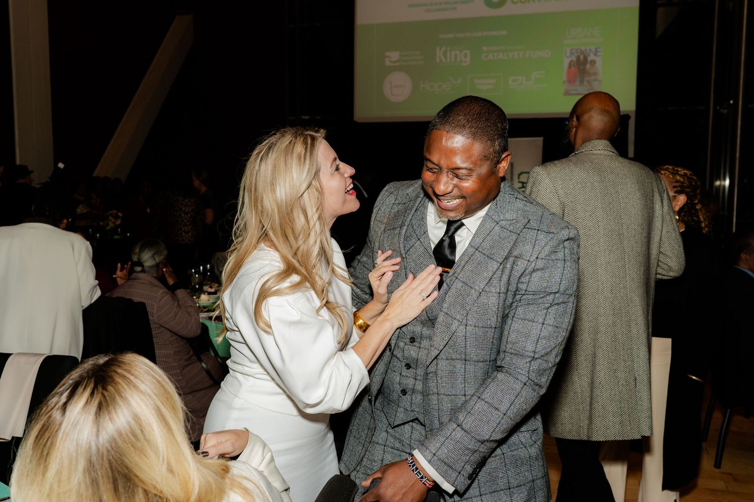 Two people sharing a lighthearted moment at a formal event.