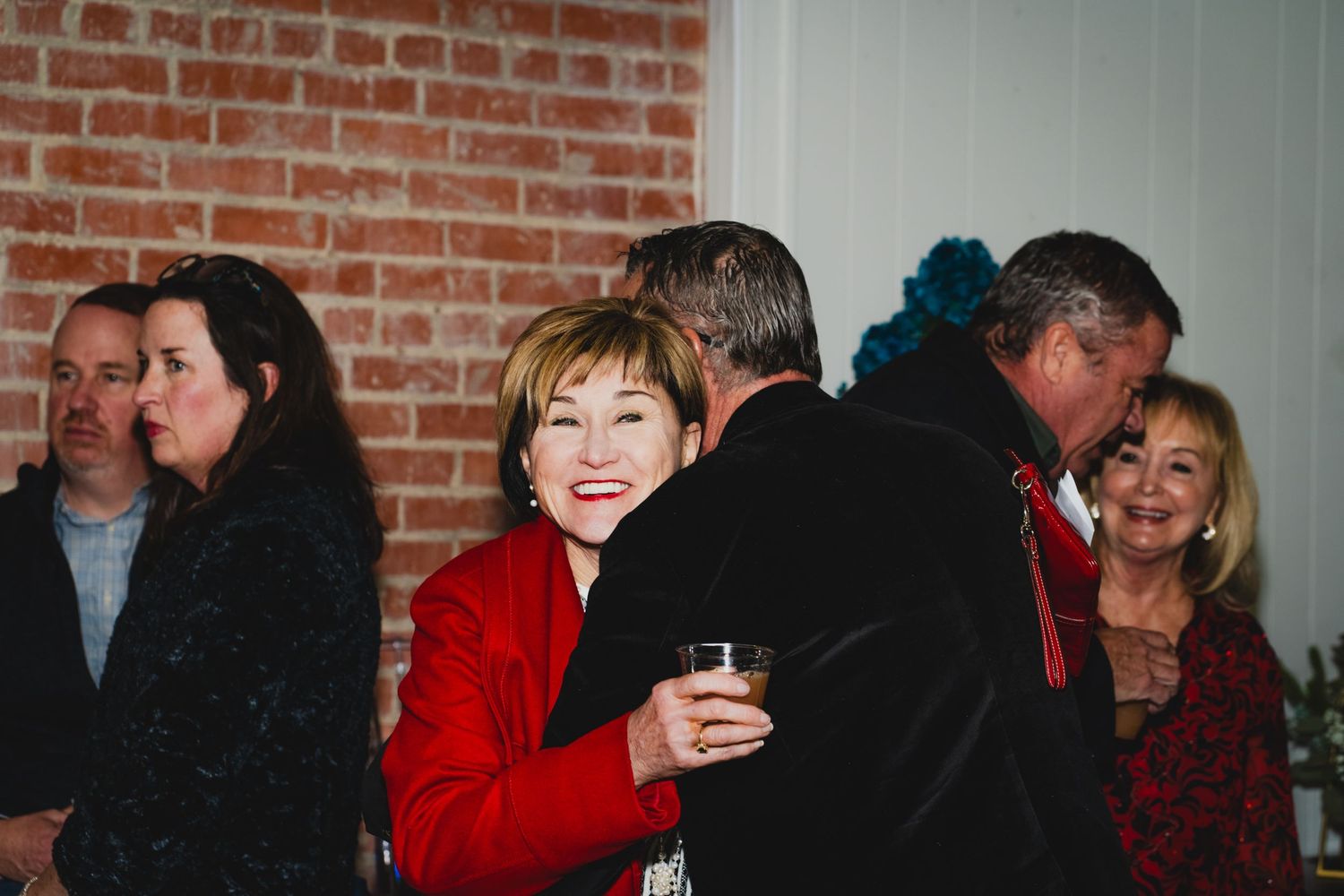 Holiday party guests gather in front of a brick wall and decorated Christmas tree.