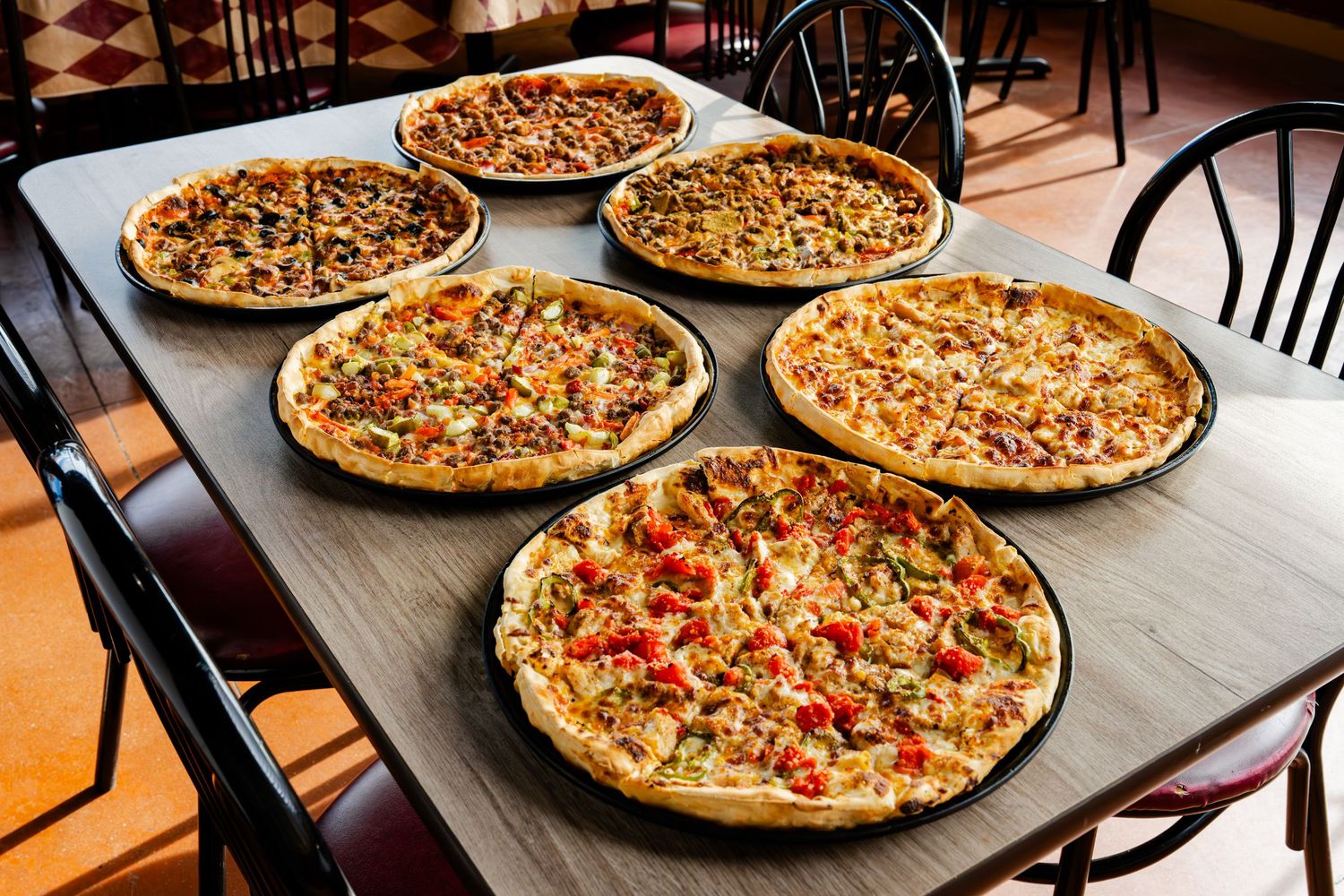 Freshly baked pizzas with various toppings arranged on metal baking sheets in a commercial kitchen setting.