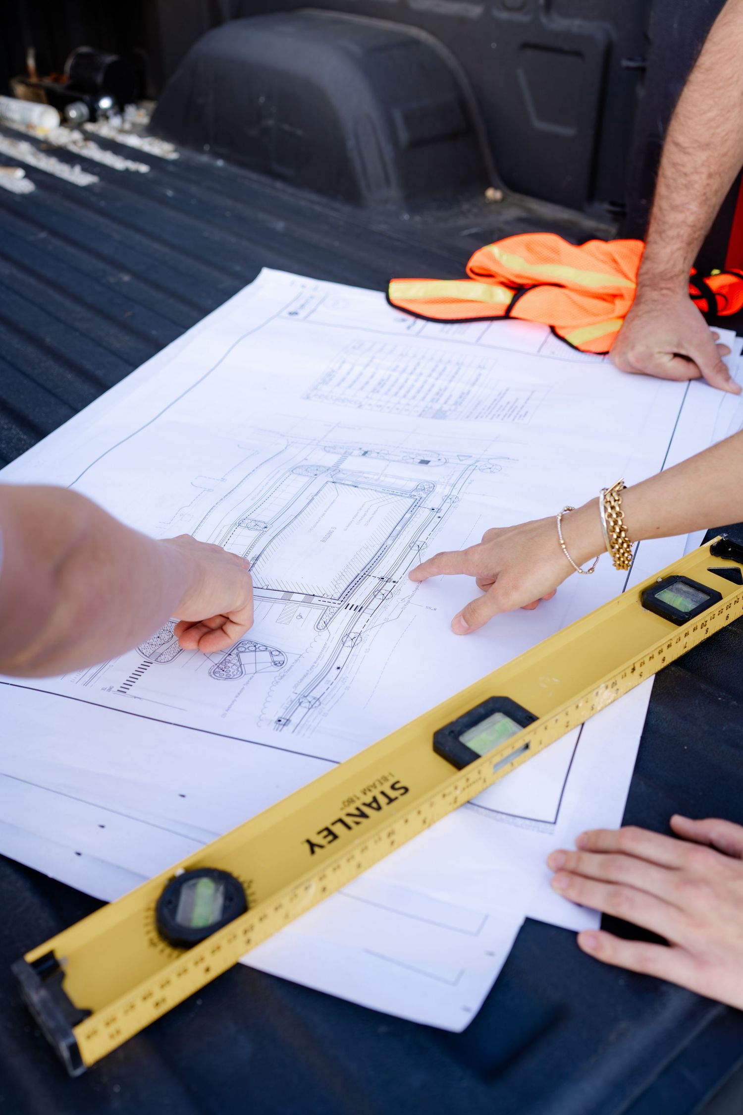 Hands point to architectural drawings while using yellow level tool for measurements.