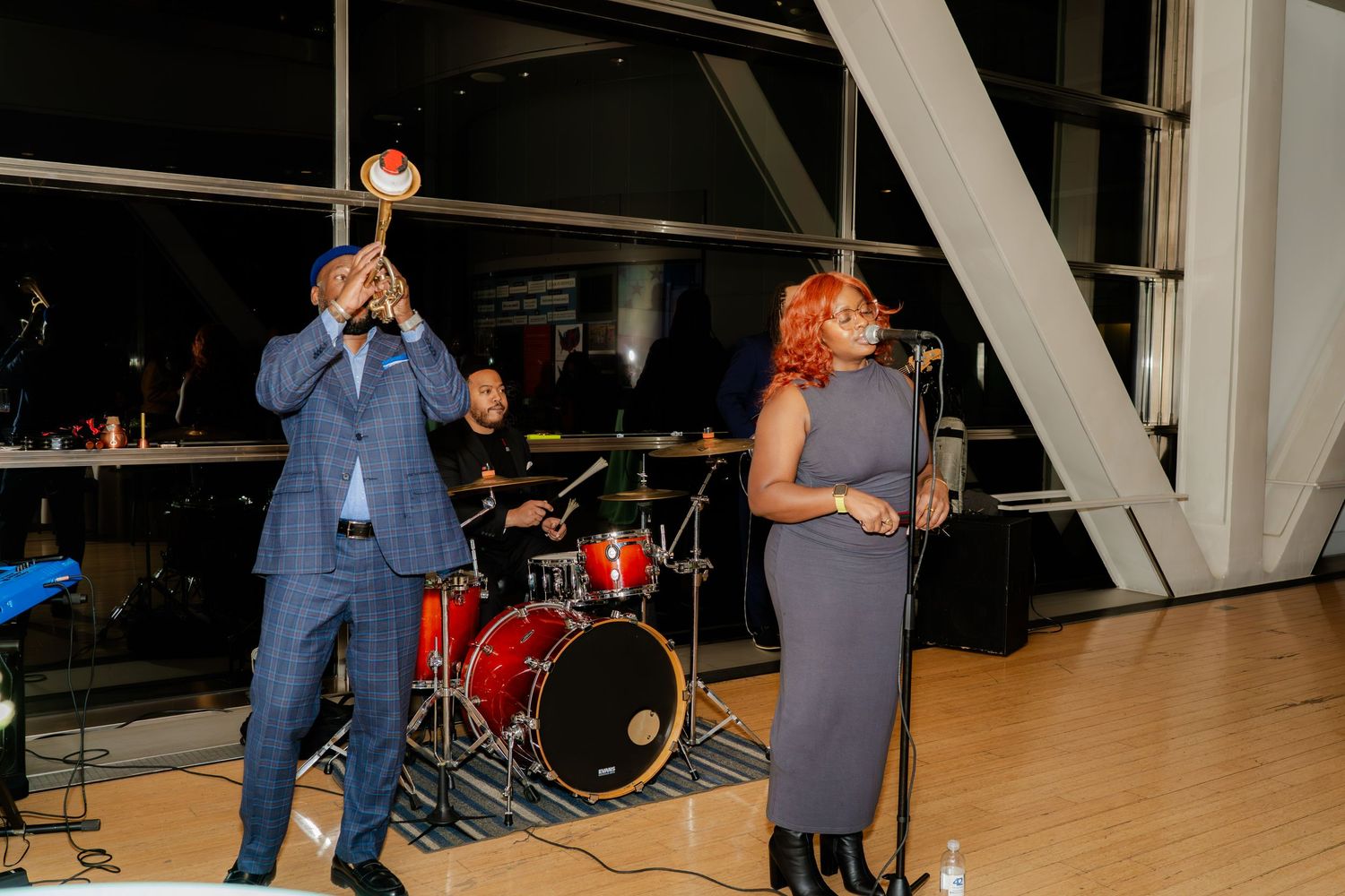Musicians performing on stage with drums and microphones at an evening event.