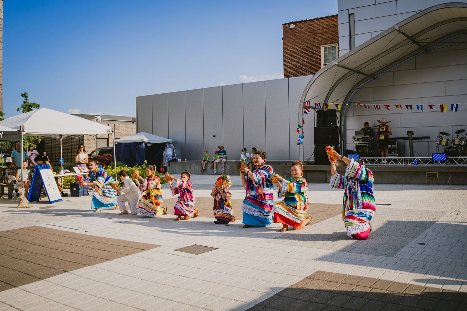 Outdoor festival scene with performance area and scattered audience members on a sunny day.