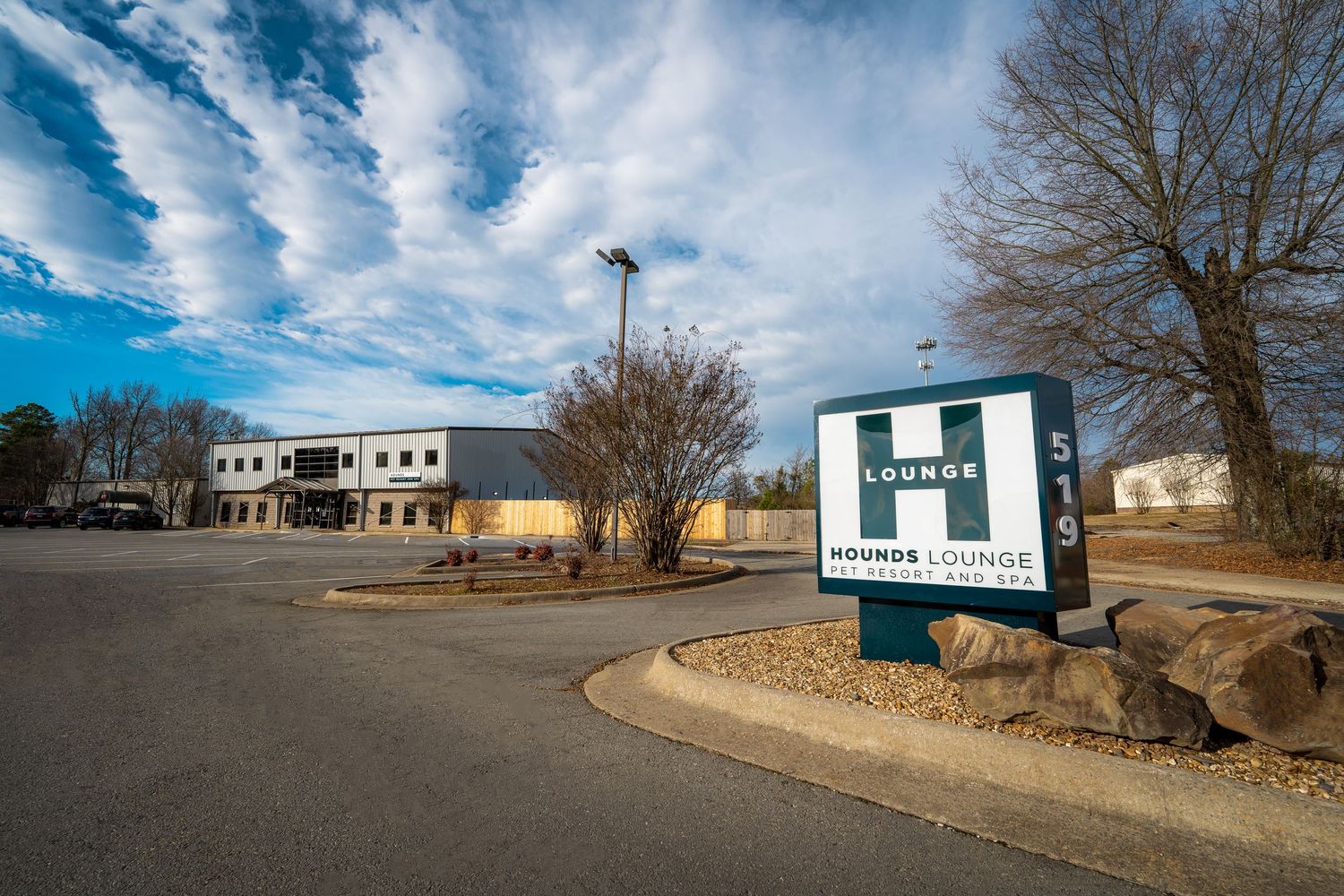 Commercial buildings and parking lot under bright blue sky with wispy clouds.