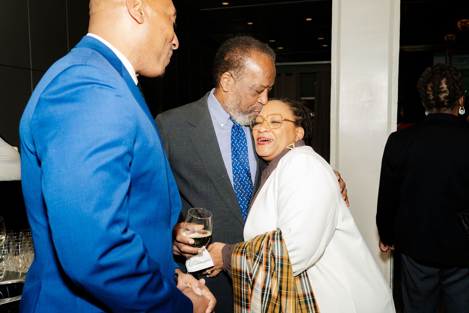 Three people engaged in conversation at an evening social event wearing formal attire.