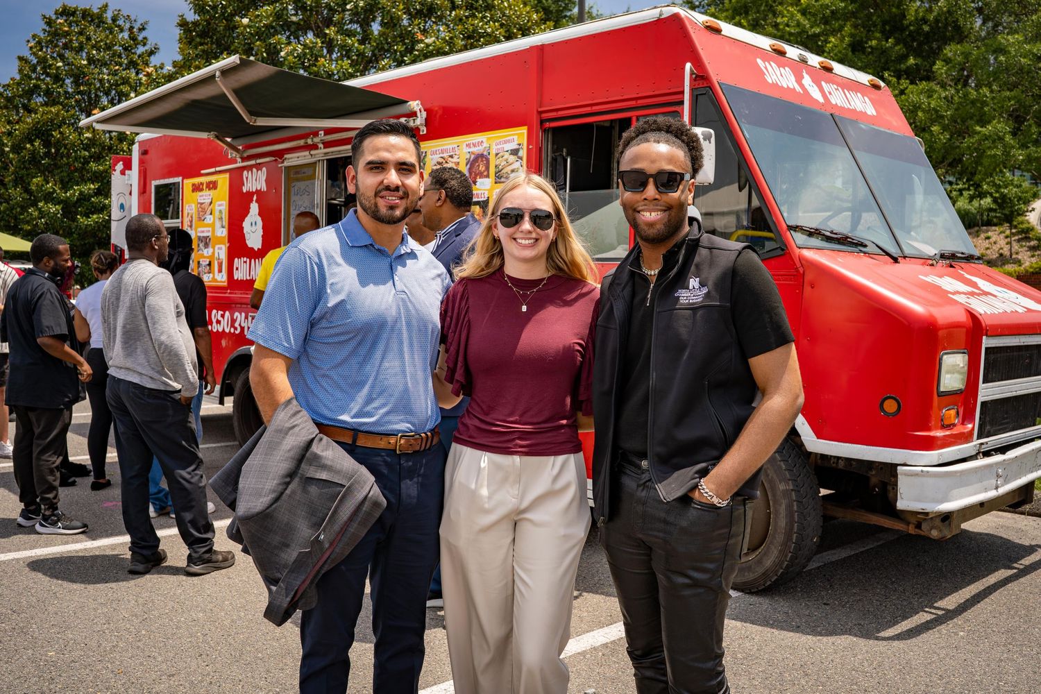 Red food truck parked at outdoor community event with attendees gathering nearby.