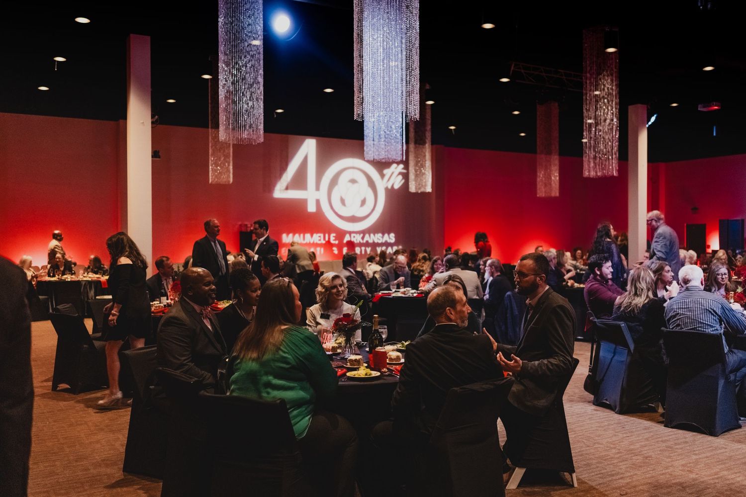 Conference attendees gather in a dimly lit venue with red accent lighting and multiple presentation screens.