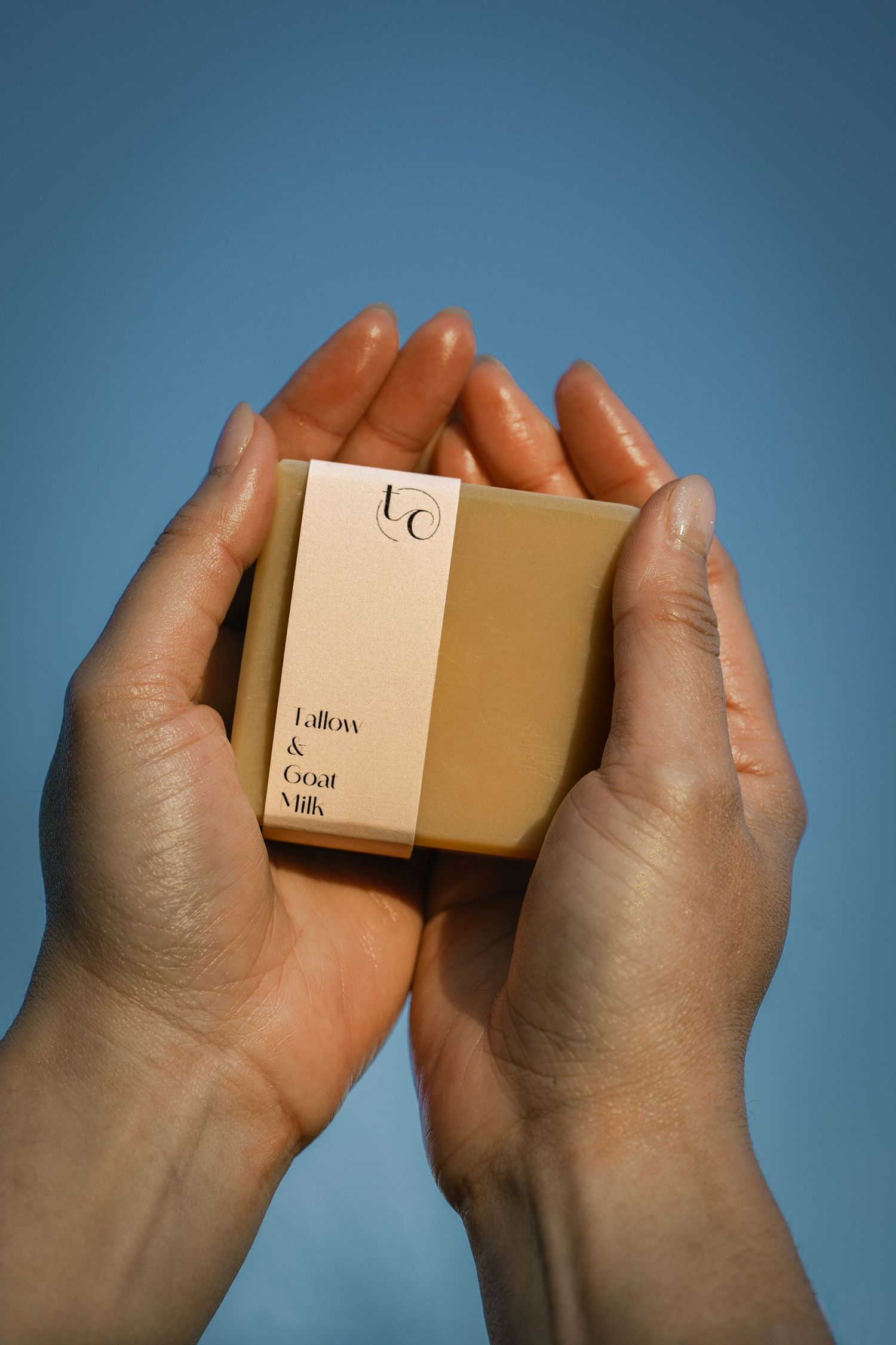 Hands holding small beige product box against blue background.