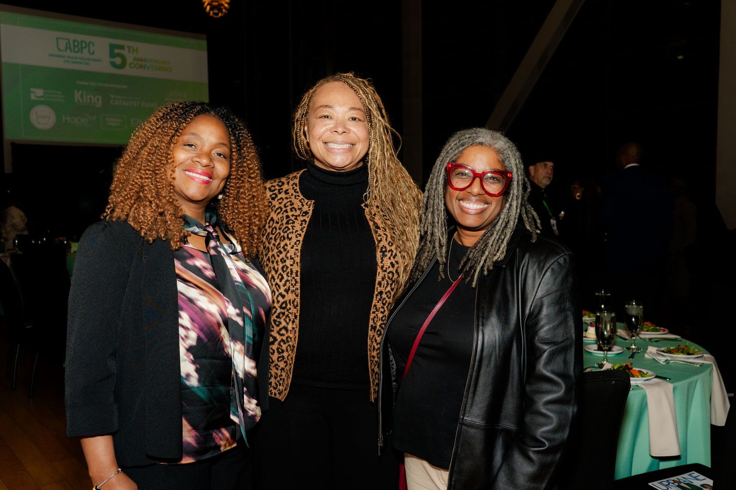 Three women pose together at an evening social gathering.