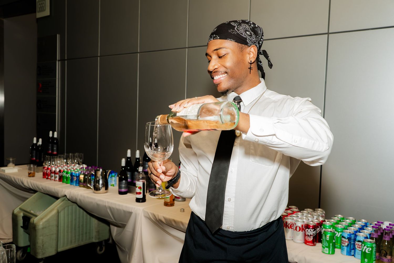 Bartender in white shirt and tie pouring drinks at an event.