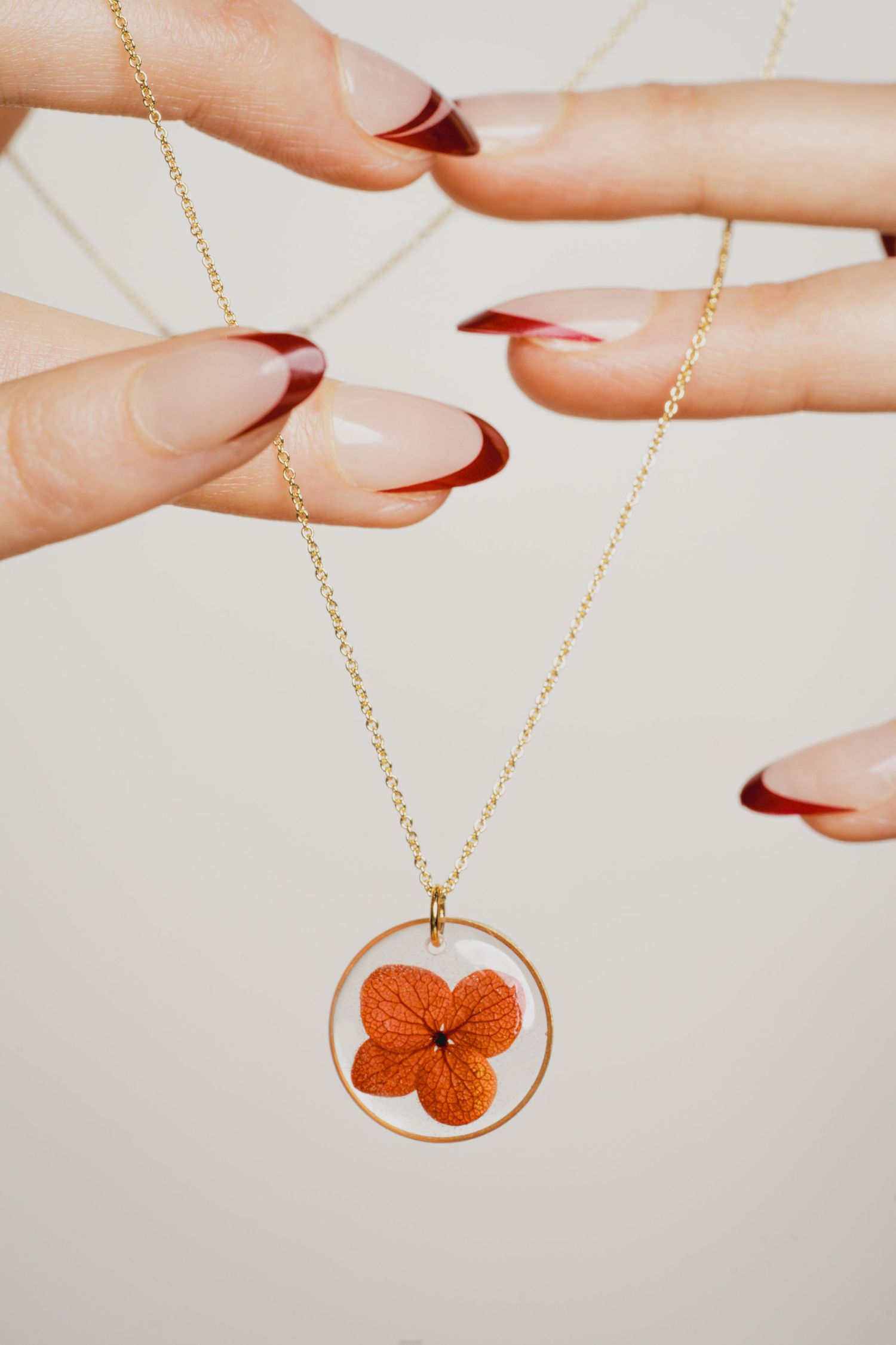 Delicate orange flower pendant necklace on gold chain displayed against white background.