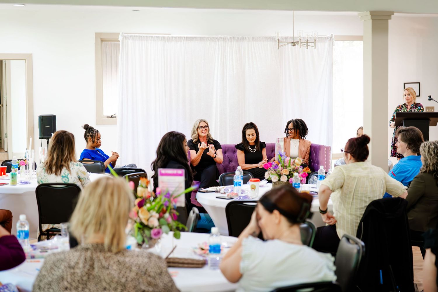 Business gathering in bright indoor space with attendees seated in rows of chairs.
