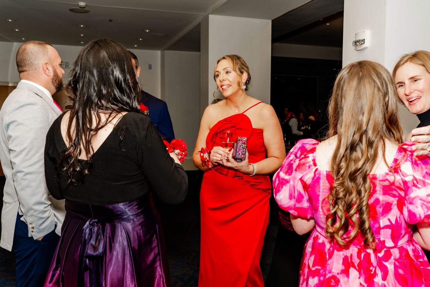 People dancing and socializing at a party with bright pink and red formal dresses.