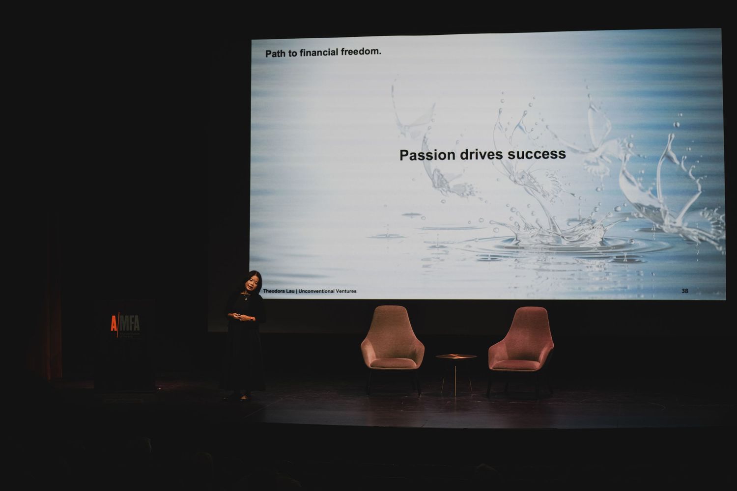 Multiple presentation screens showing business-related text in a dark auditorium.