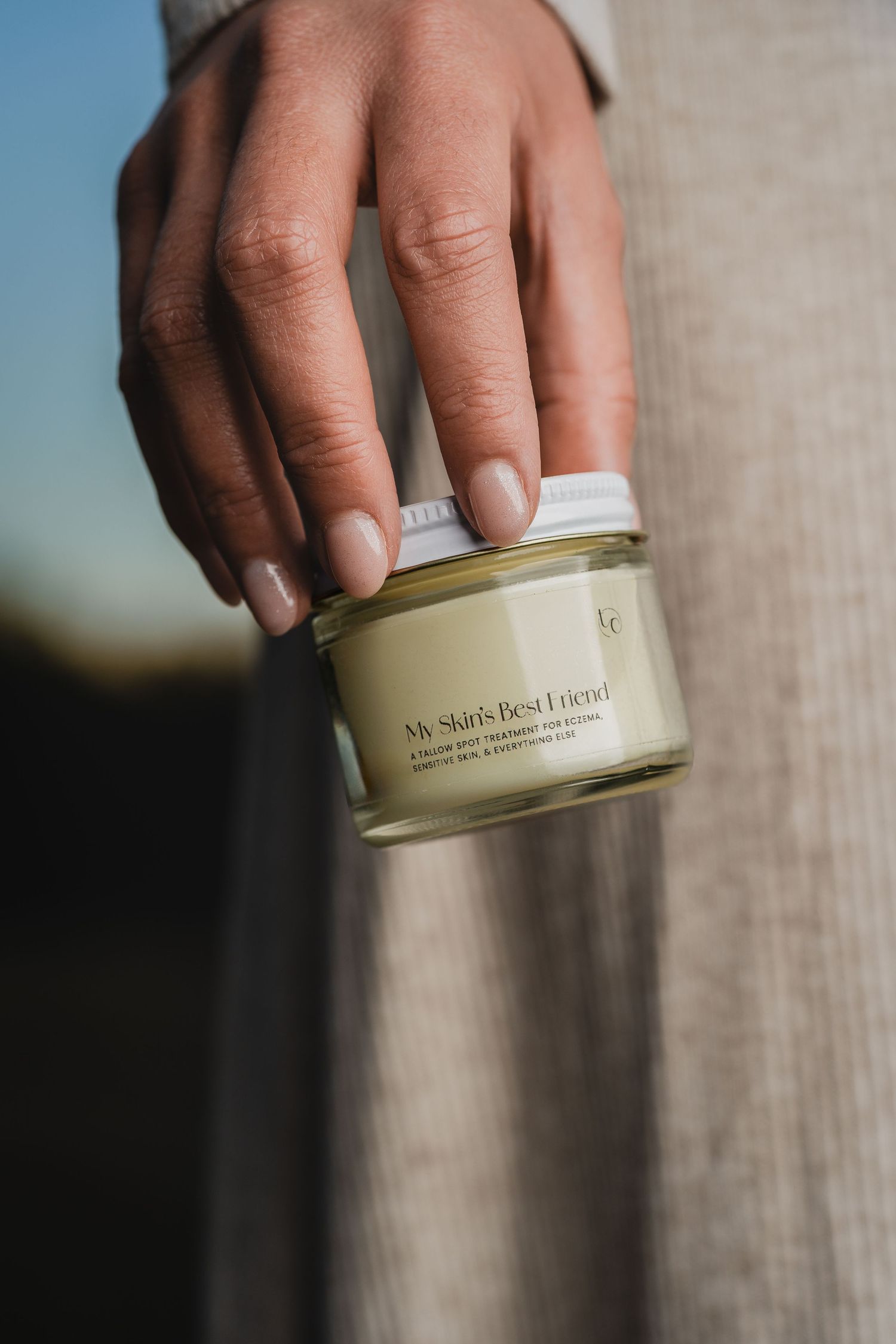 Hands holding and displaying a cylindrical cream product container against neutral background.