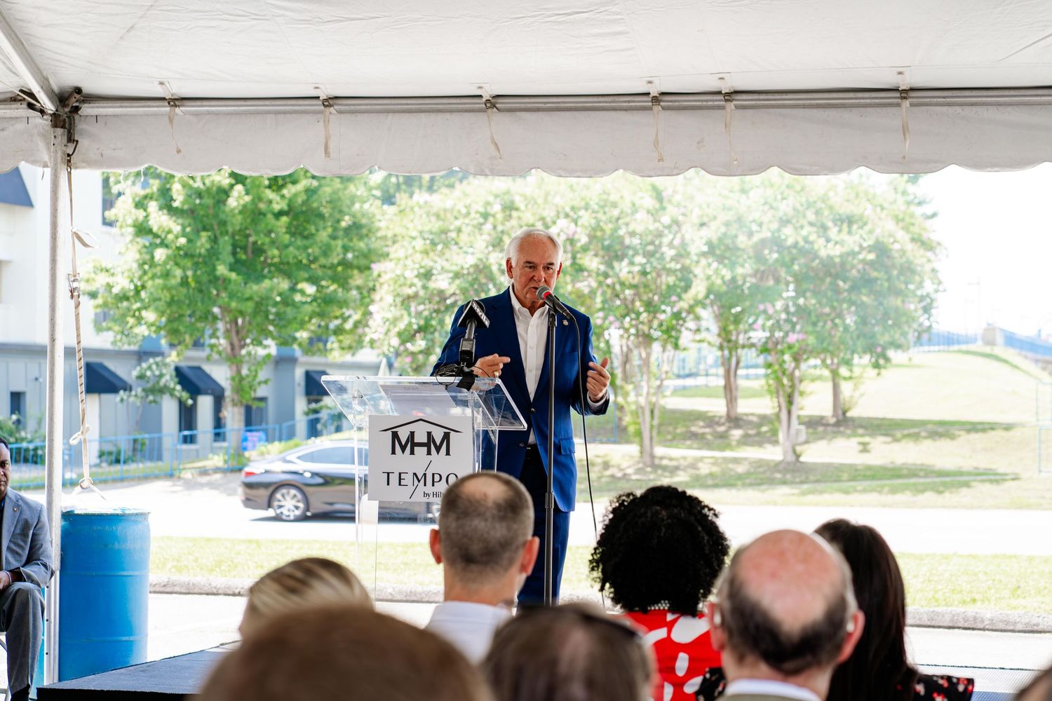 Crowd gathered under white canopy tent during outdoor daytime event.