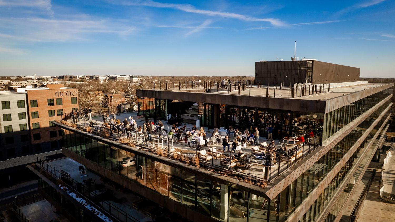 Panoramic cityscape view of urban buildings and rooftops under a bright blue sky.