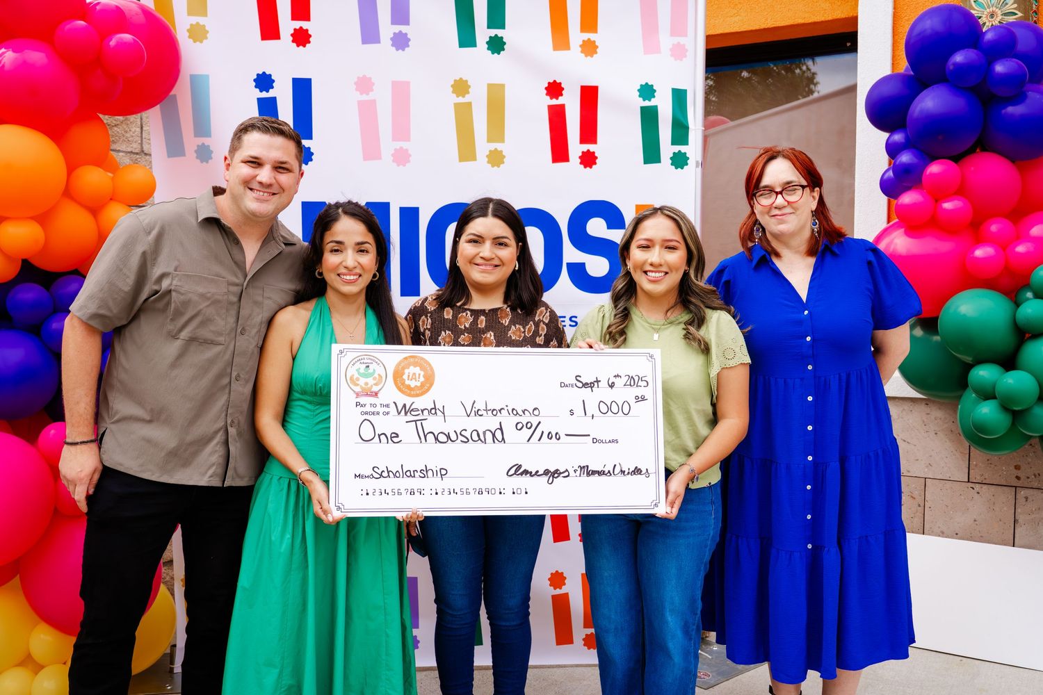 Event attendees gathered around large presentation check at Amigos facility opening.