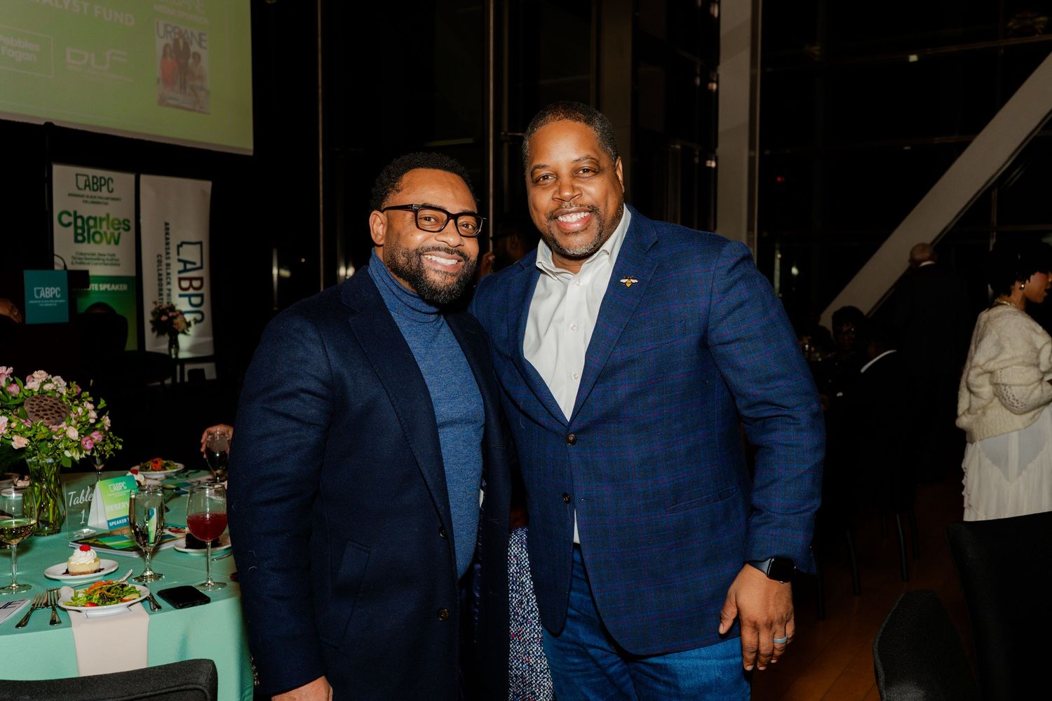Two men in business attire pose together at a formal event.