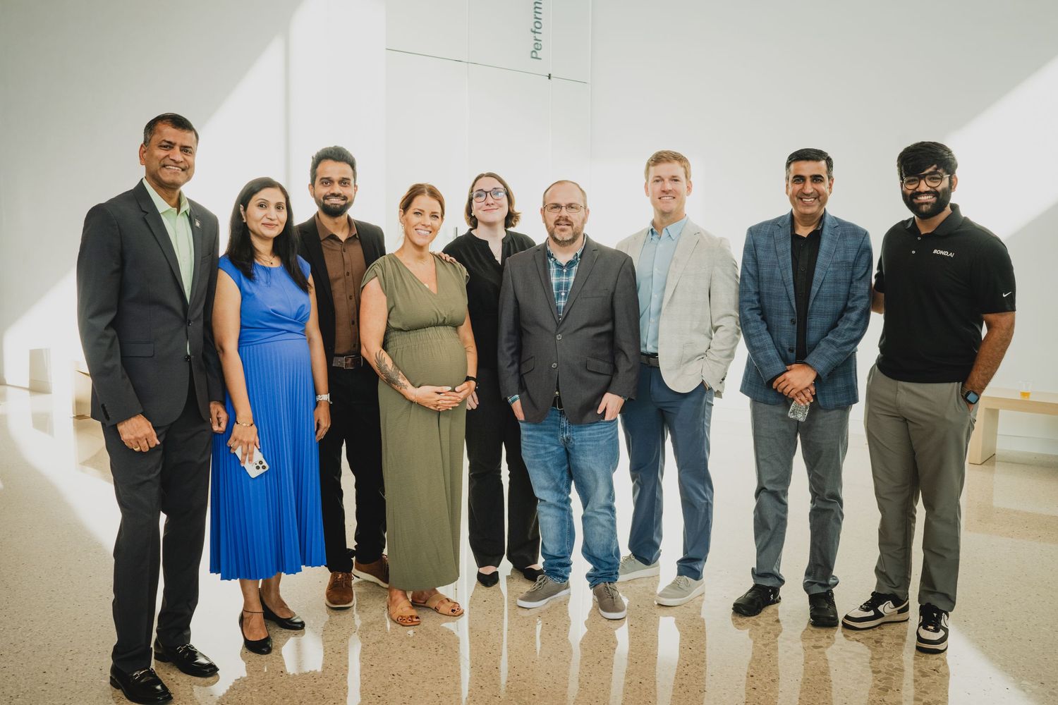 A row of professionally dressed people standing together against a white wall at an event.