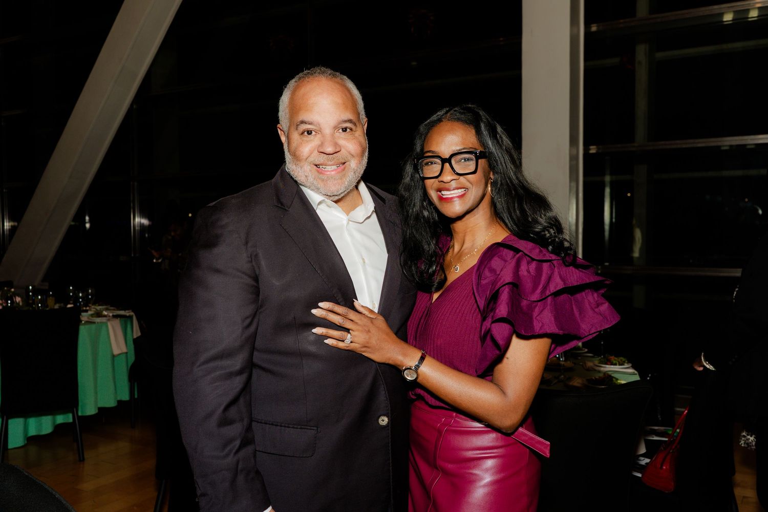 A couple posing together at an evening event, with the woman wearing a vibrant purple dress.