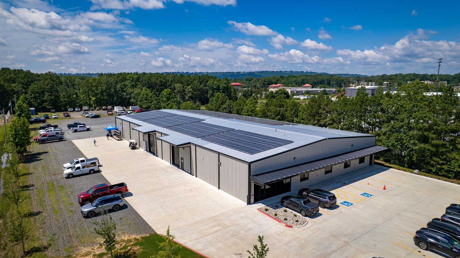 Industrial warehouse building with solar panels on roof and parked cars in front.