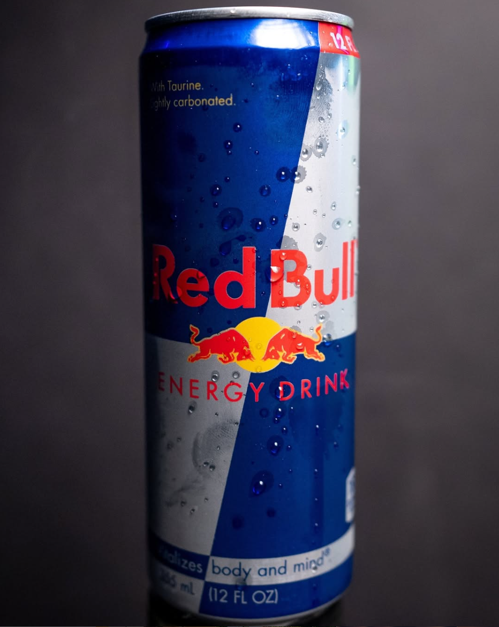 Red Bull energy drink can with condensation against dark background.