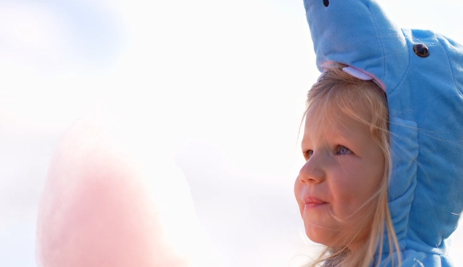 Child wearing blue shark hat against bright sky background.
Halloween. trick or treating. trunk or treat. cotton candy.