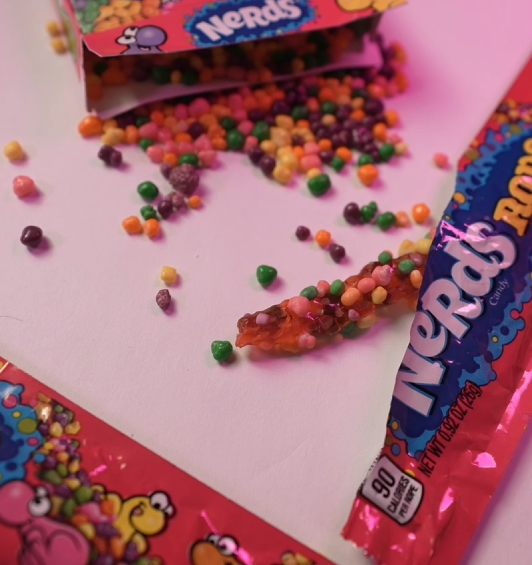 Nerds candy pieces spilled from package on pink background.