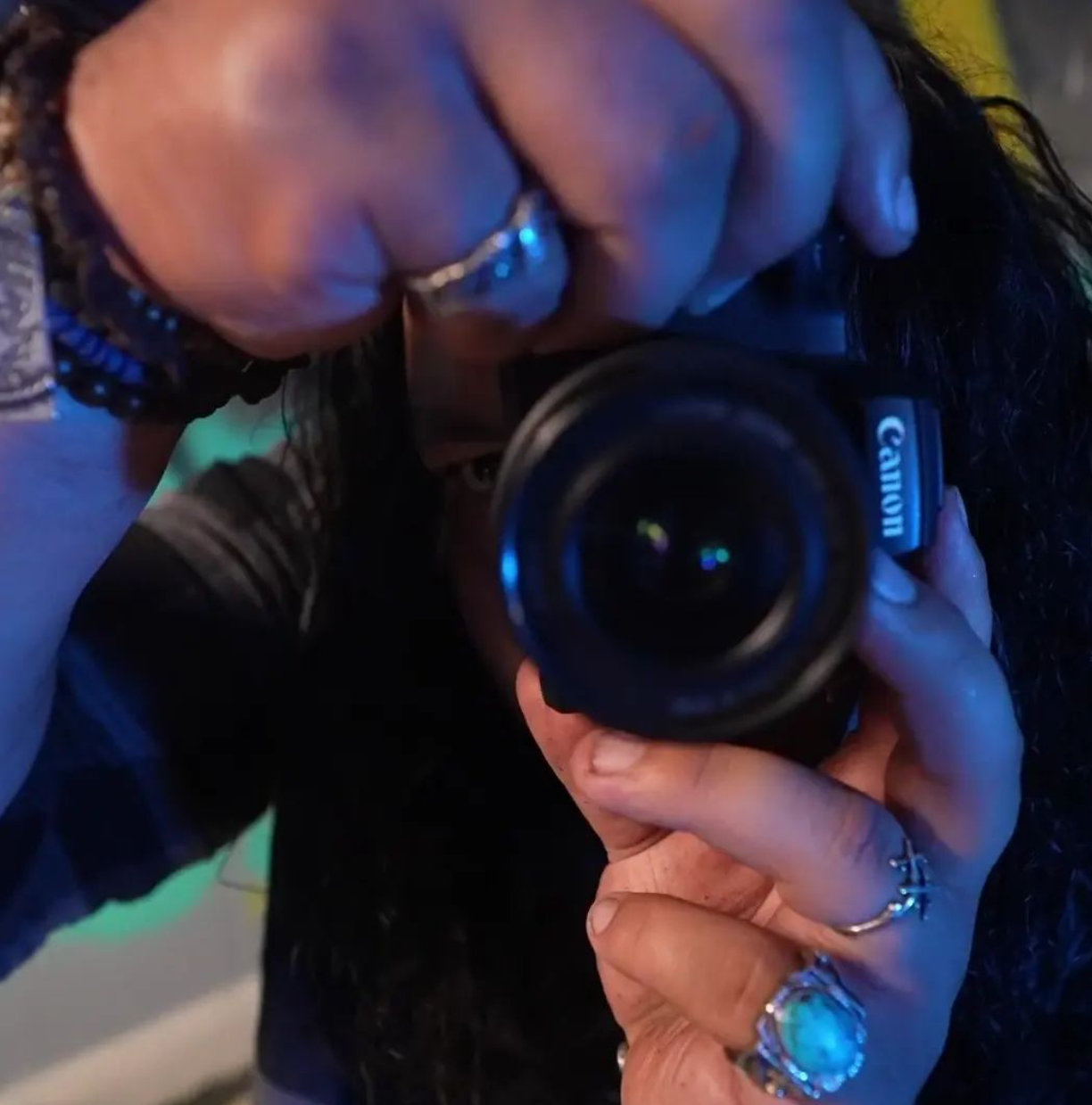 Close-up of hands holding Canon camera lens in blue lighting.