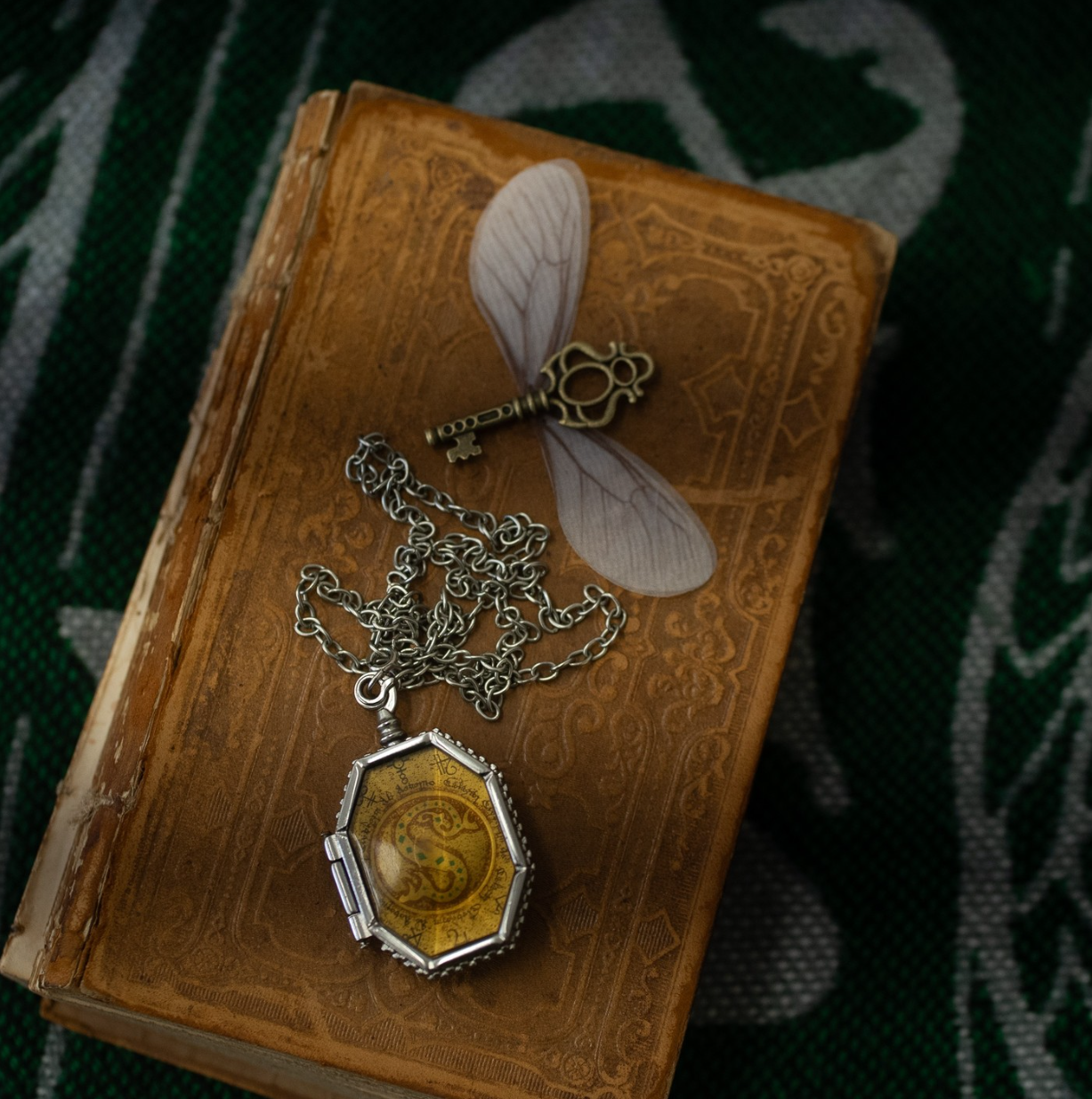 Close-up of an old leather-bound book with ornate gold pendant on silver chain. harry potter. Slytherin Horcrux