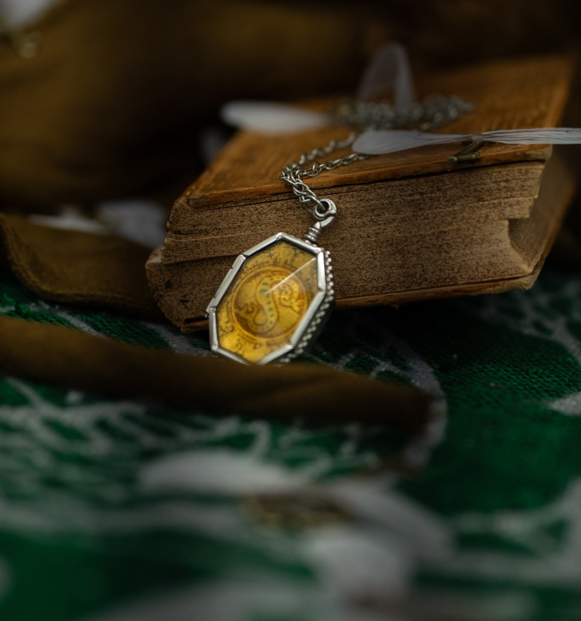 Vintage book with antique gold pendant necklace and delicate butterfly decorations on dark green background. Harry potter. Slytherin horcrux